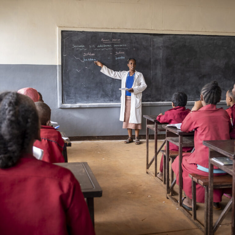 Eine Lehrerin spricht vor ihrer Klasse. Die Schülerinnen und Schüler hören gespannt zu.