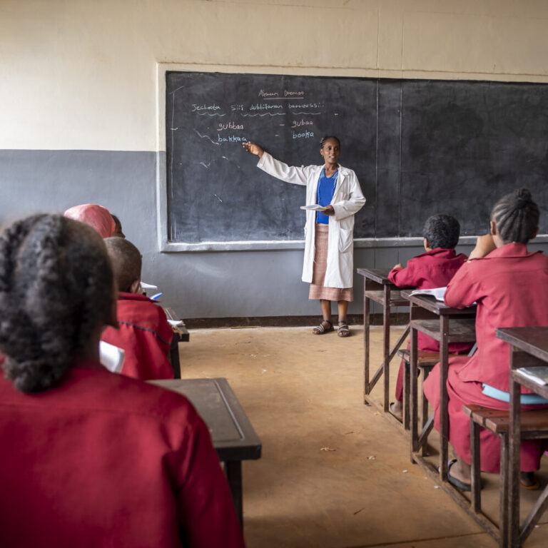 Eine Lehrerin spricht vor ihrer Klasse. Die Schülerinnen und Schüler hören gespannt zu.