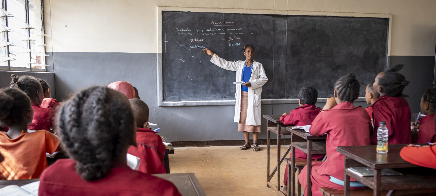 Eine Lehrerin spricht vor ihrer Klasse. Die Schülerinnen und Schüler hören gespannt zu.