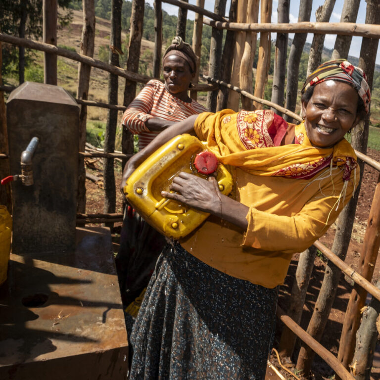 Zwei Frauen füllen gelbe Kanister mit Wasser und unterstützen damit den Zugang ländlicher Gemeinden zu sauberem Wasser.