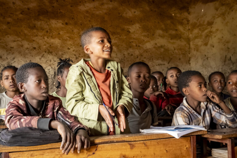 Schülerinnen und Schüler nehmen in einem verfallenen Klassenzimmer am Unterricht teil.