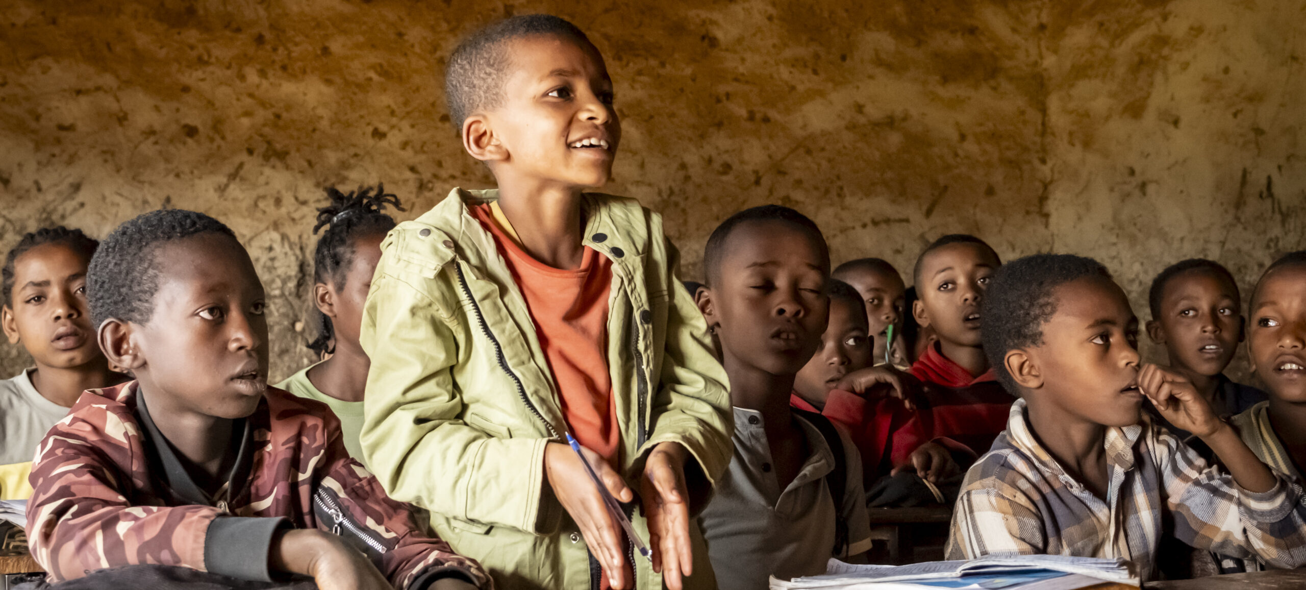 Schülerinnen und Schüler nehmen in einem verfallenen Klassenzimmer am Unterricht teil.
