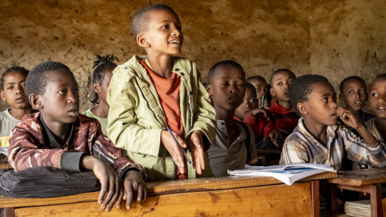 Schülerinnen und Schüler nehmen in einem verfallenen Klassenzimmer am Unterricht teil.