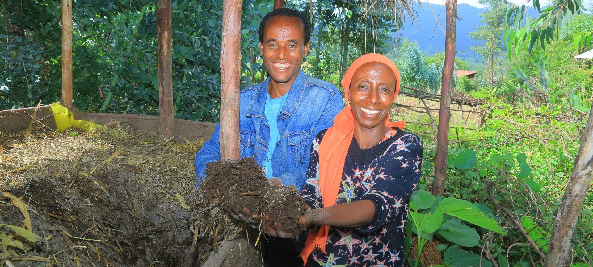 Eine Frau und ein Mann die lächelnd Erde in die Kamera halten.