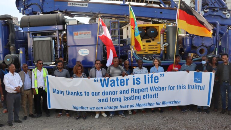 Team das vor dem mobilen Bohrgerät steht mit äthiopischer und deutscher Flagge und einem Banner mit der Schrift 