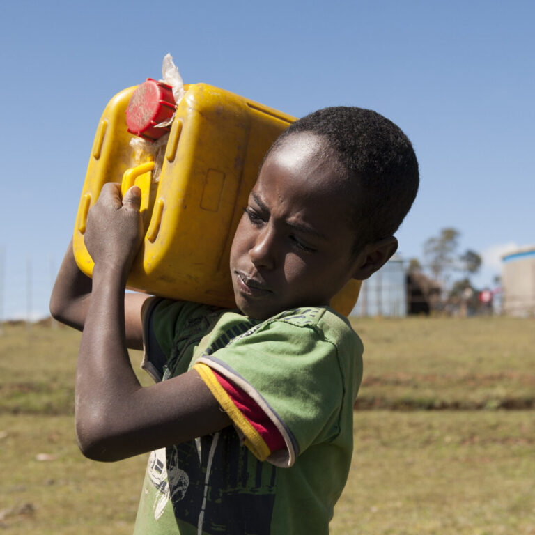 Junge trägt gelben Wasserkanister auf Schulter