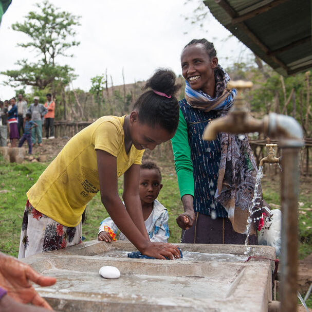 Frauen und Mädchen waschen an der neuen Wasserstelle ihre Wäsche.