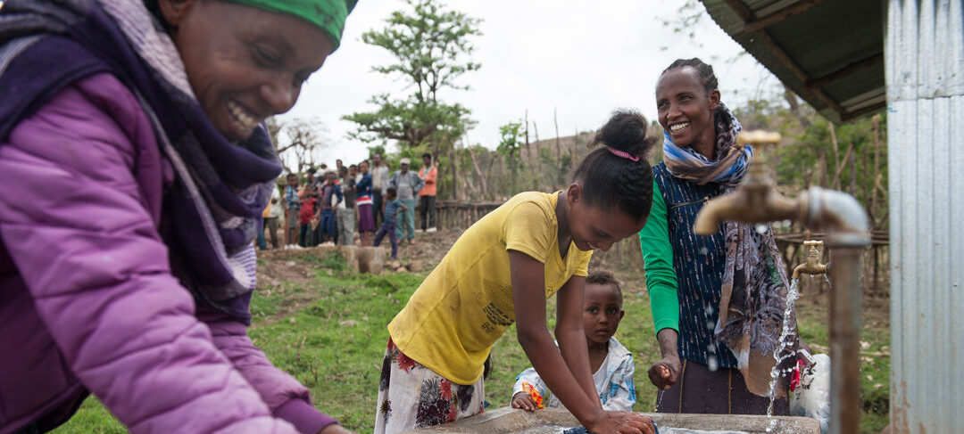 Frauen und Mädchen waschen an der neuen Wasserstelle ihre Wäsche.