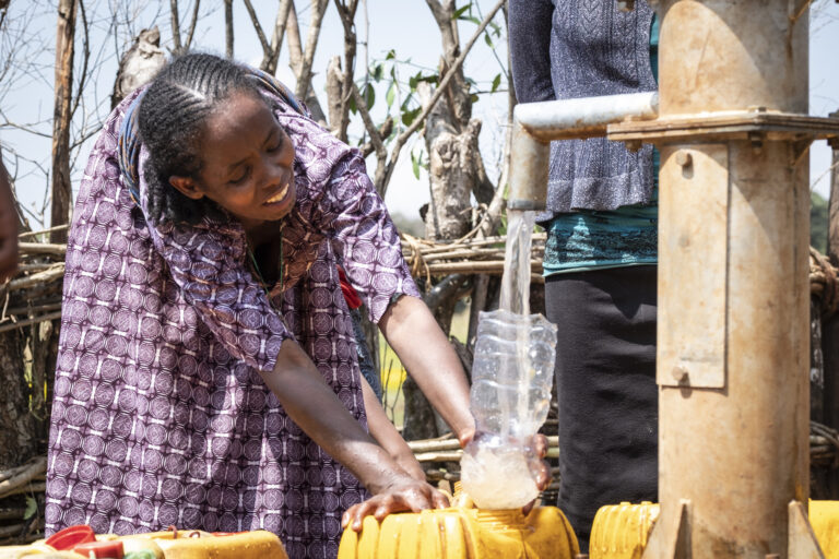 Eine Frau bückt sich und füllt mit einem Trichter ihren Wasserkanister an einem Brunnen auf.