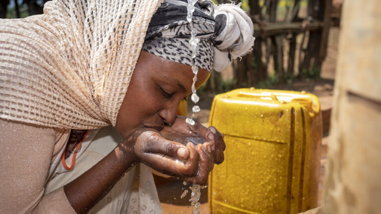 Eine Frau trinkt sauberes Wasser aus einem neu gebauten Brunnen.