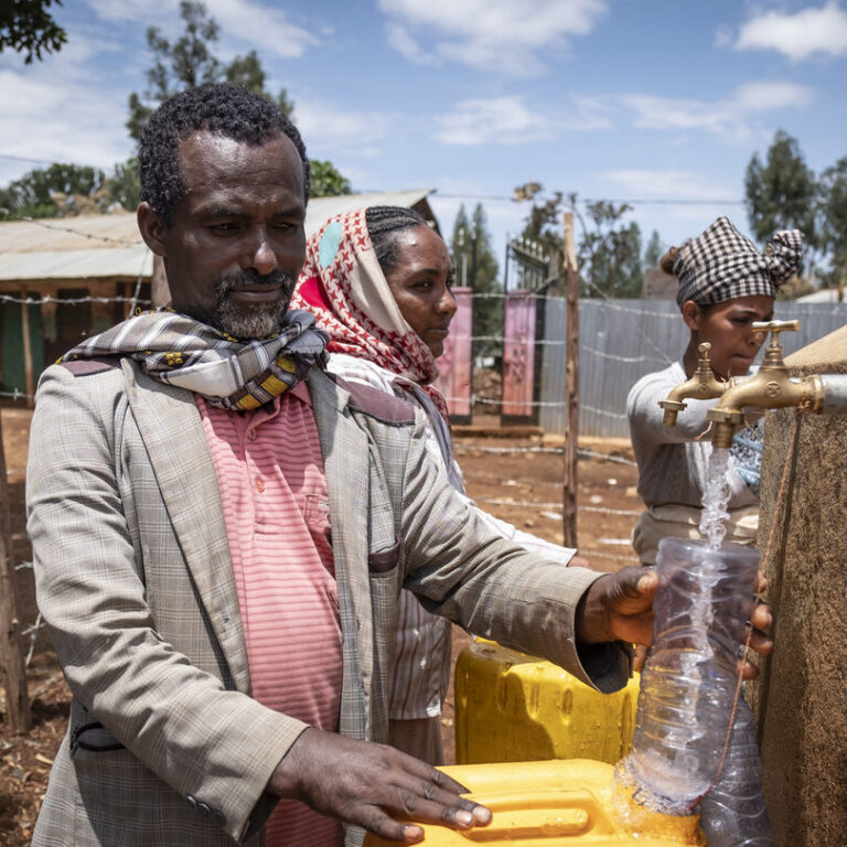 Ein Mann der an einem Brunnen Wasser in seinen Kanister füllt.