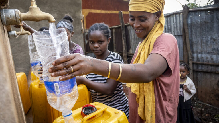 Eine Frau füllt an einem Wasserbrunnen Wasser in ihren Kanister.