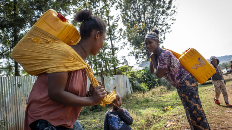 Frauen tragen Wasserkanister auf ihrem Rücken.