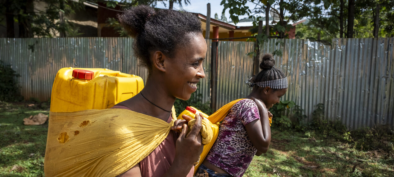 Zwei Frauen laufen mit Wasserkanistern auf dem Rücken.