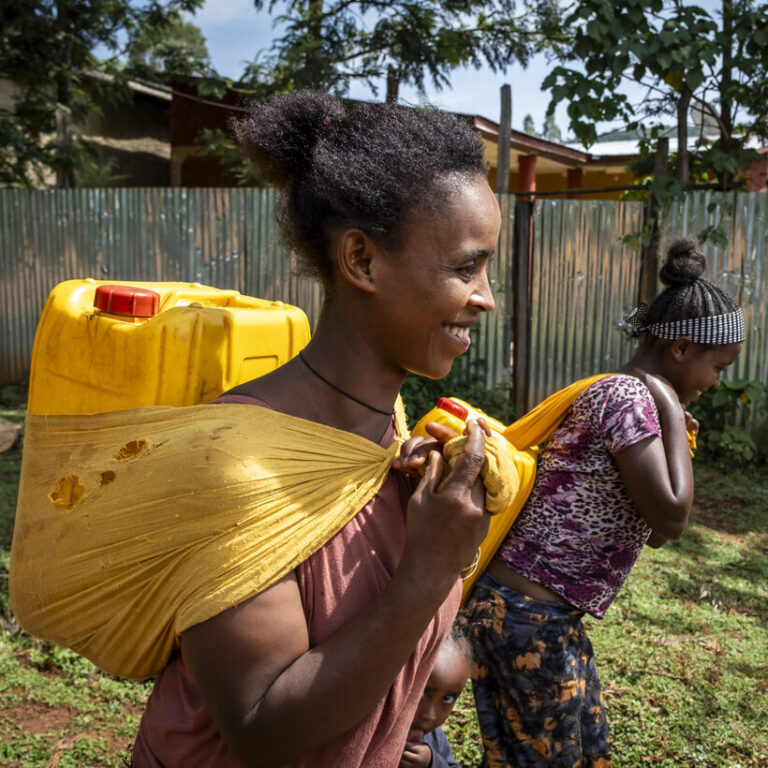 Zwei Frauen laufen mit Wasserkanistern auf dem Rücken.