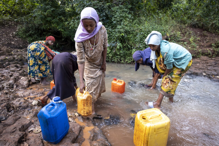 Eine Gruppe von Frauen die in einem Fluss ihre Wasserkanister auffüllen.