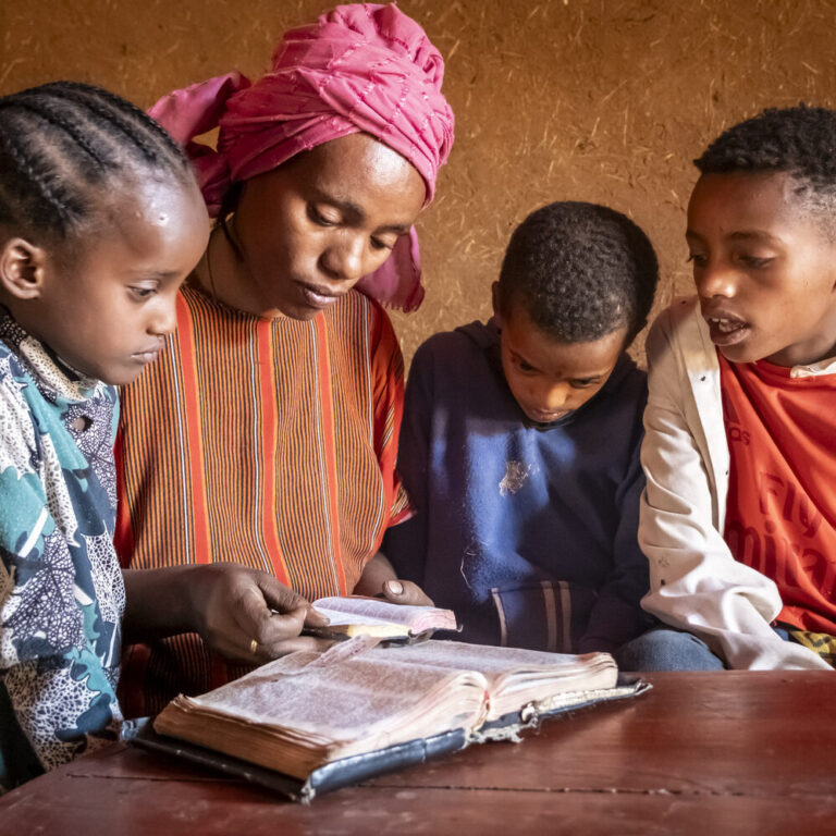 Eine Mutter und drei Kinder schauen zusammen in ein aufgeschlagenes Buch.