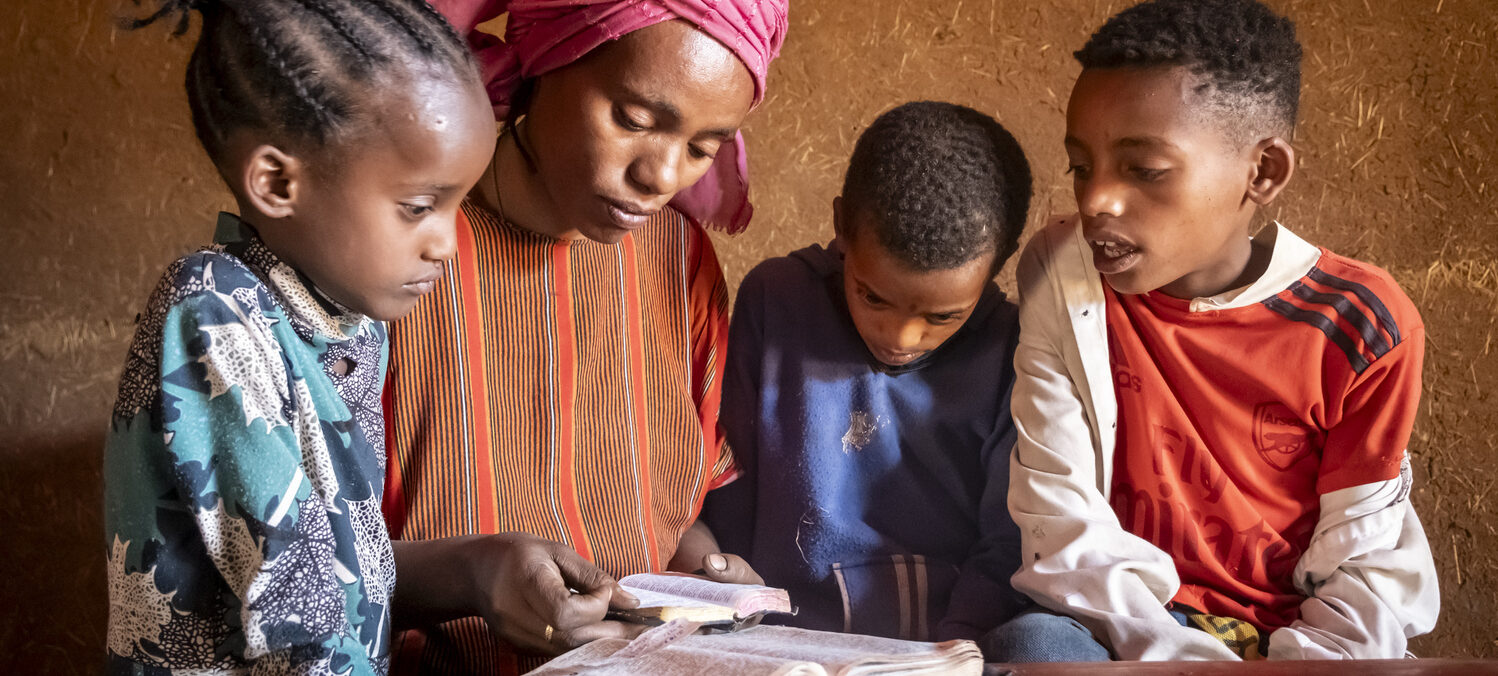 Eine Mutter und drei Kinder schauen zusammen in ein aufgeschlagenes Buch.