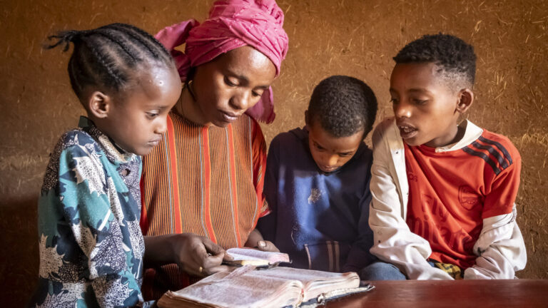 Eine Mutter und drei Kinder schauen zusammen in ein aufgeschlagenes Buch.