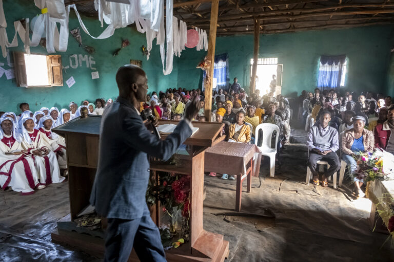 Ein Priester hält eine Predigt vor einem Raum voller Menschen.