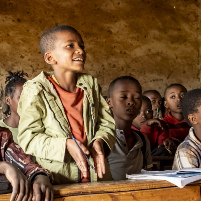 Schülerinnen und Schüler nehmen in einem verfallenen Klassenzimmer am Unterricht teil.