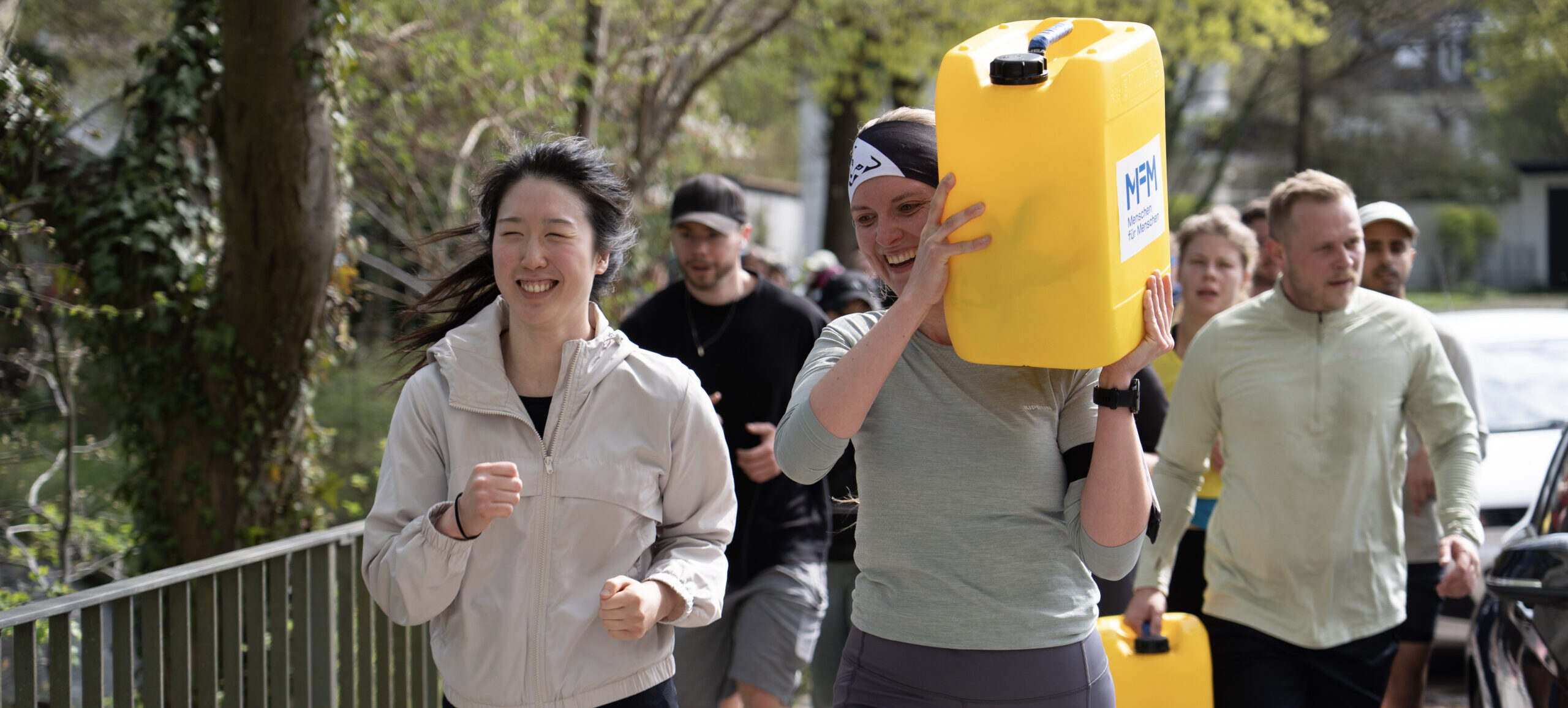 Lachende Frau läuft mit Wasserkanister auf Schulter.