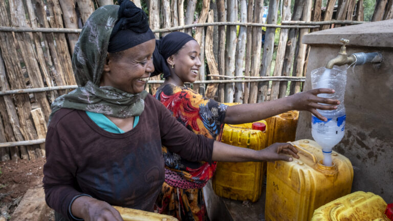 Zwei Frauen füllen frisches Trinkwasser in gelbe Kanister ab.