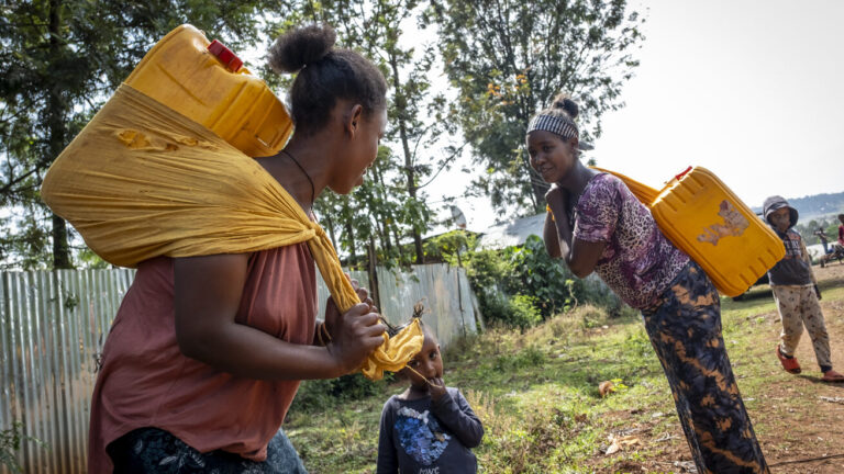 Zwei Frauen in Äthiopien, die Wasserkanister auf dem Rücken tragen.