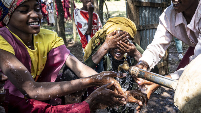 Ein Kind wäscht sich aus einer neuen Wasserquelle das Gesicht.