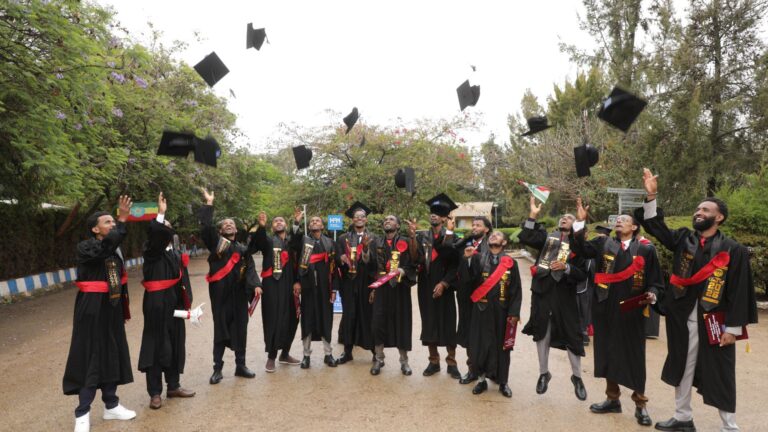Studierende vom ATTC die in einem halbkreis stehen in ihren schwarzen Abschlussoben und ihren Hut in die Luft werfen.