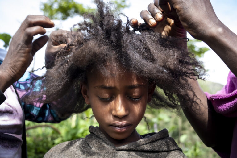 Frontalansicht eines Mädchens, die ihre Haare geflochten bekommt.