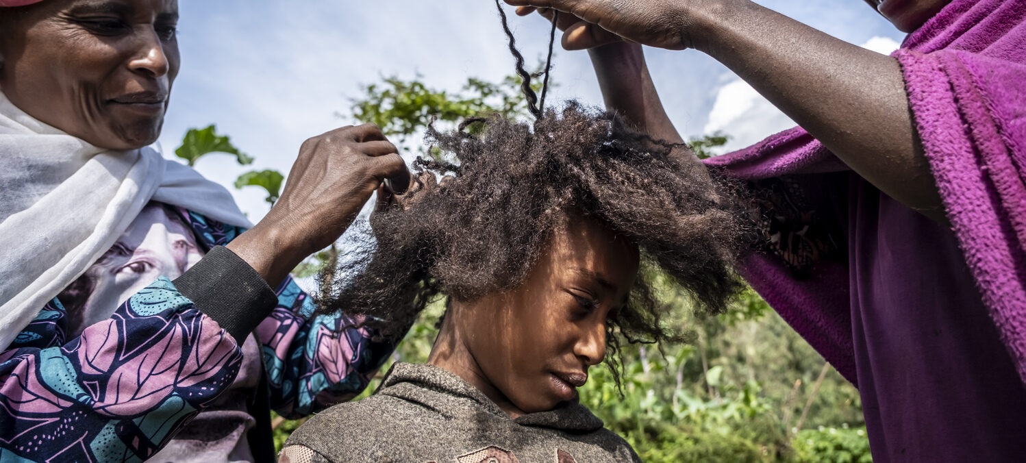 Zwei Frauen die einem jungen Mädchen eine Frisur flechten.