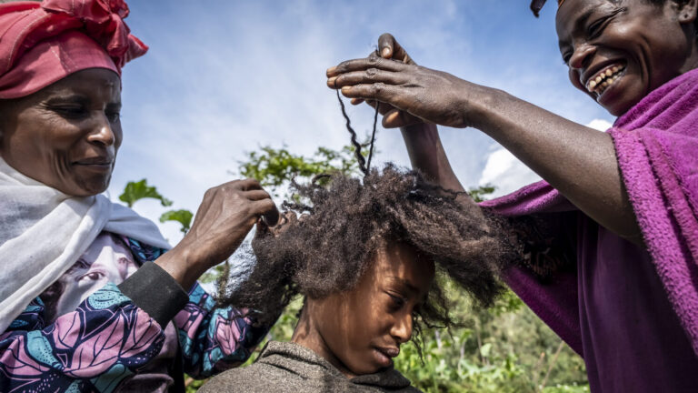 Zwei Frauen die einem jungen Mädchen eine Frisur flechten.