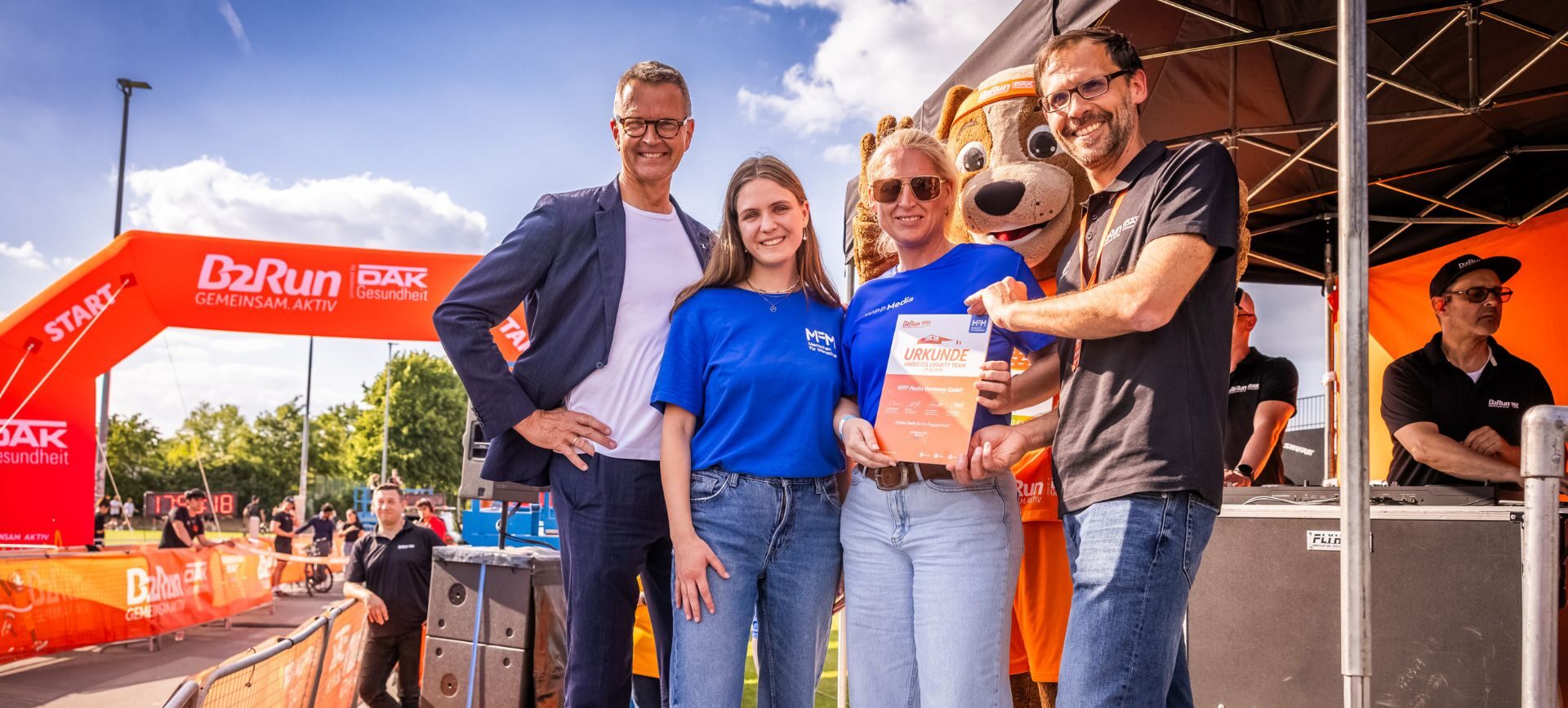 Zwei Männer, zwei Frauen, die auf einem Podest stehen und eine Urkunde in die kamera halten. Beim B2Run.
