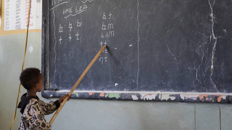 Junge zeigt mit Holzstab auf Buchstaben an einer Tafel