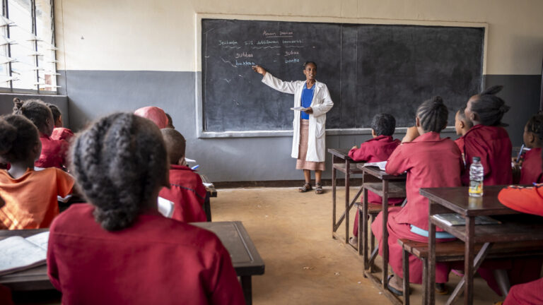 Eine Lehrerin spricht vor ihrer Klasse. Die Schülerinnen und Schüler hören gespannt zu.