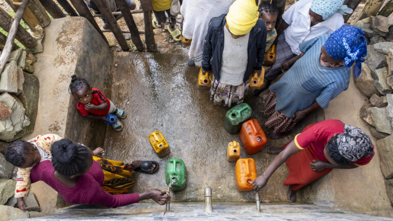 Bild von oben. Frauen stehen am Brunnen und lassen ihre Kanister mit Wasser befüllen.