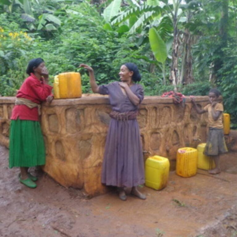 Zwei junge Frauen unterhalten sich beim Wasserholen mit Kanistern an einer Wasserstelle.